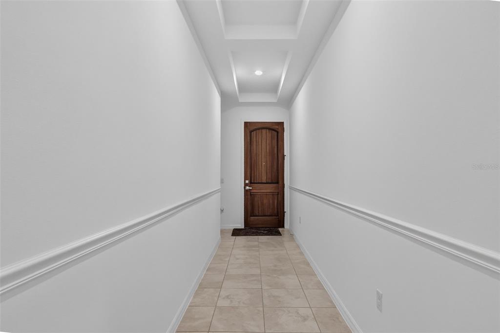 A hallway with white walls, chair rail molding, tile flooring, and a wooden front door — 14681 SETON CREEK BOULEVARD, WINTER GARDEN, FL
