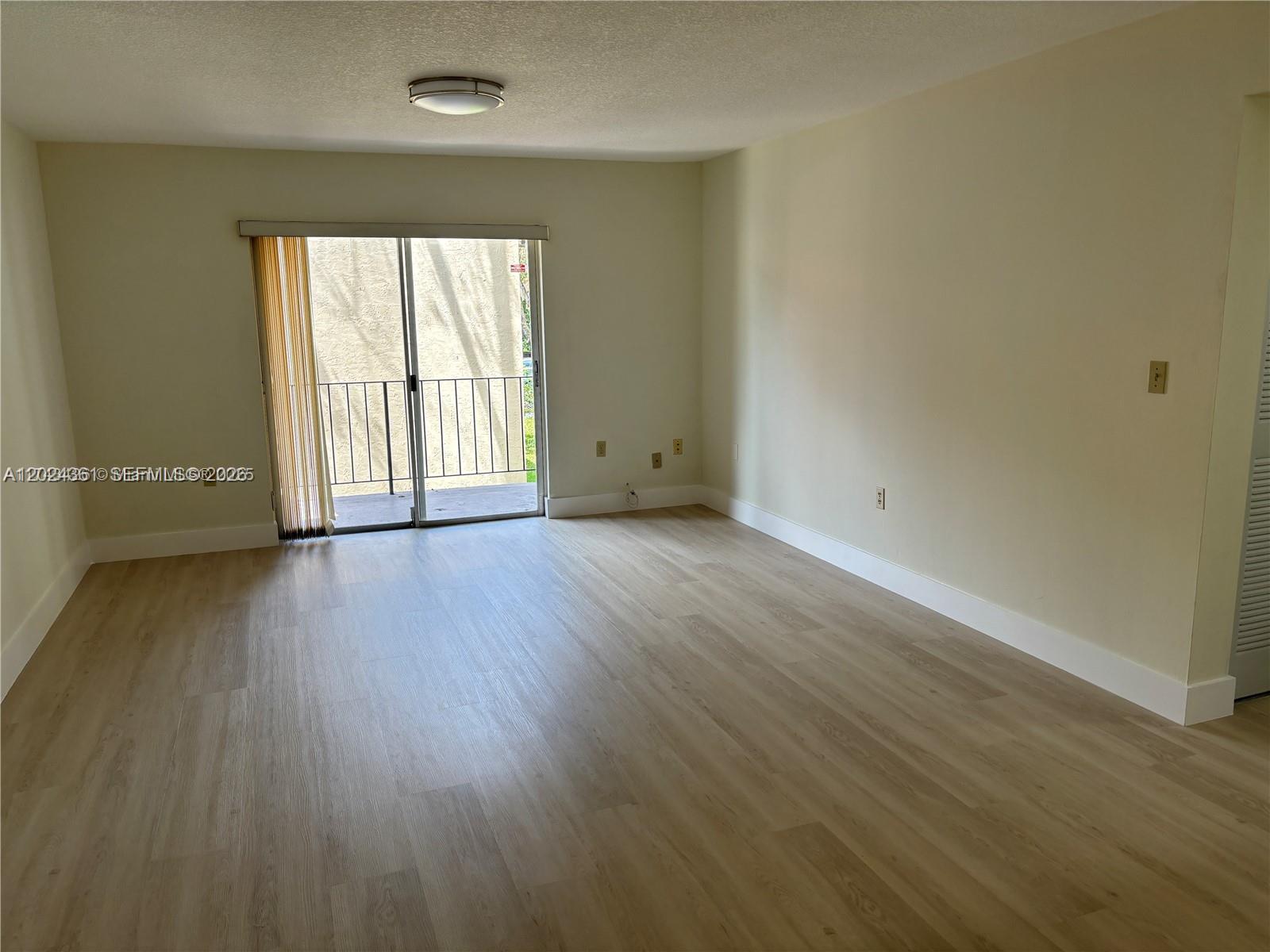An empty living room features light wood-look flooring, beige walls, and a sliding glass door — 10744 N Kendall # 18, Miami FL 33176, MIAMI, FL