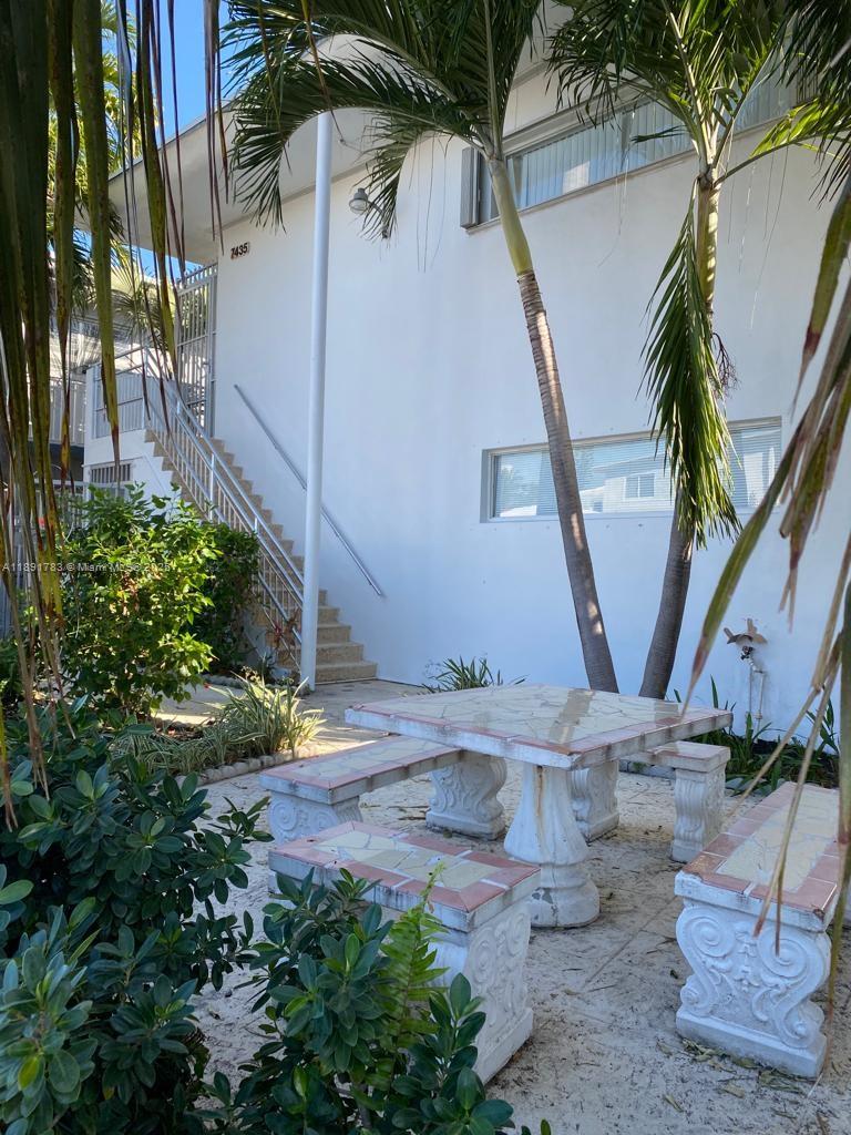 A white building exterior features a stone table and benches on a sandy patio area — 7435 Byron Ave, Miami Beach FL 33141, MIAMI BEACH, FL