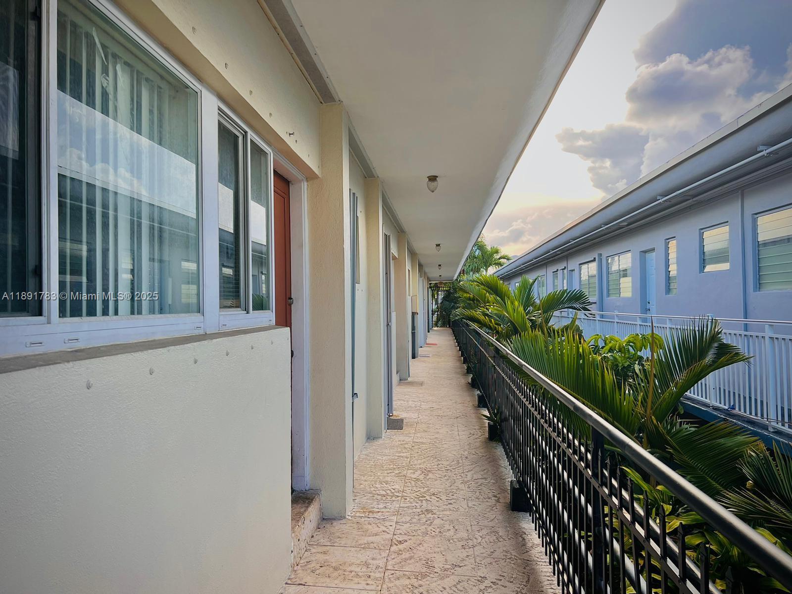 An outdoor walkway with tile flooring runs between two apartment buildings with metal railings — 7435 Byron Ave, Miami Beach FL 33141, MIAMI BEACH, FL