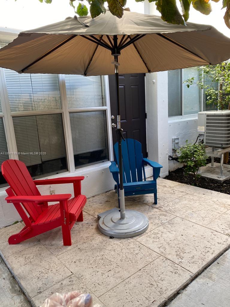 A patio features a tan umbrella, a red Adirondack chair, and a blue Adirondack chair — 7435 Byron Ave, Miami Beach FL 33141, MIAMI BEACH, FL