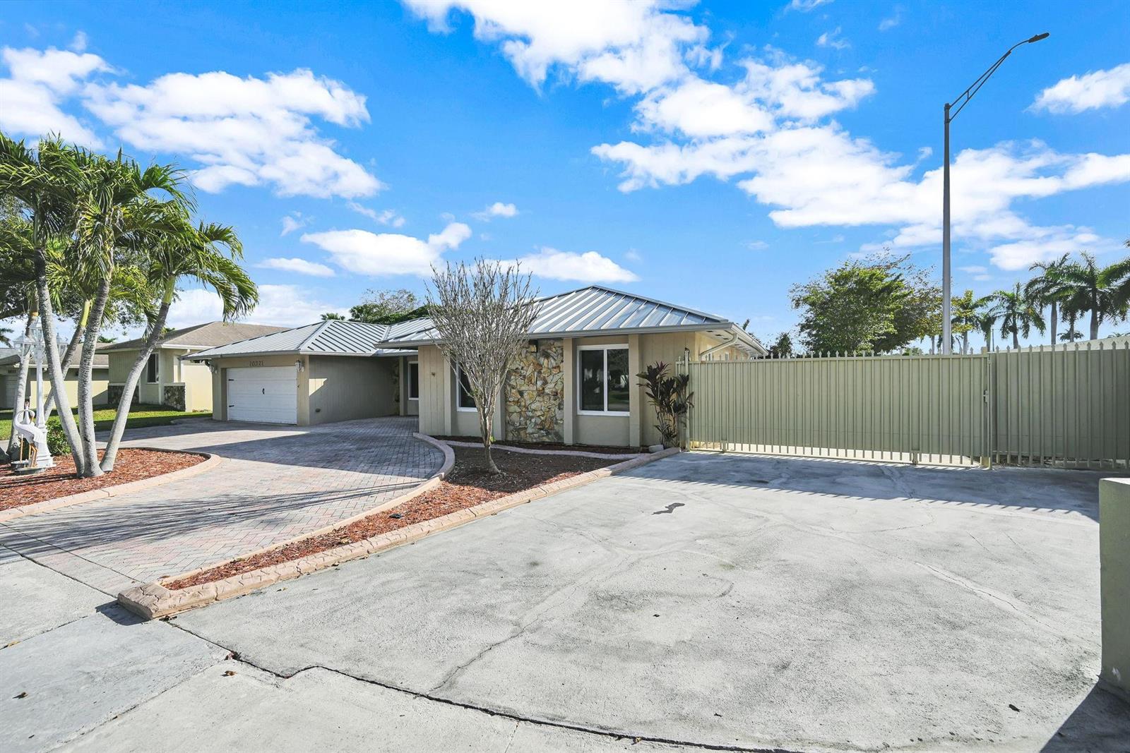 A single-story house features a metal roof, stone facade, paved driveway, and a gated entrance — 10321 SW 116th Avenue, Miami FL 33176, MIAMI, FL