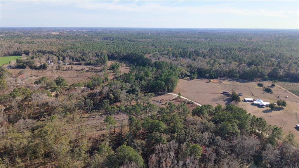 An aerial view shows a rural landscape with wooded areas, open fields, and a small house — 14403 NW 258TH PLACE, ALACHUA, FL