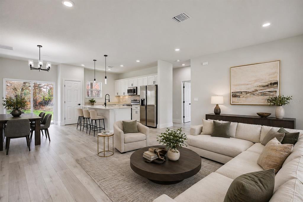 An open-concept living room and kitchen featuring light wood floors and neutral-toned furniture — 5230 SAN JUAN DRIVE, SEBRING, FL