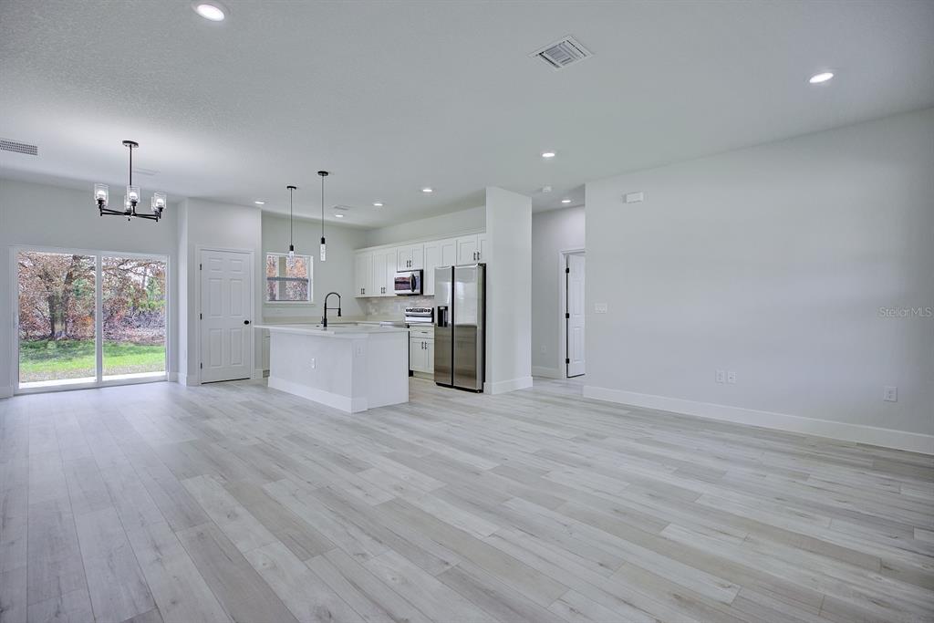 A bright, open-concept kitchen and living area features white cabinetry, stainless appliances, and light flooring — 5230 SAN JUAN DRIVE, SEBRING, FL