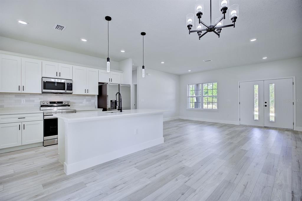 A modern kitchen with white cabinets, a central island, and light wood-look flooring — 5230 SAN JUAN DRIVE, SEBRING, FL