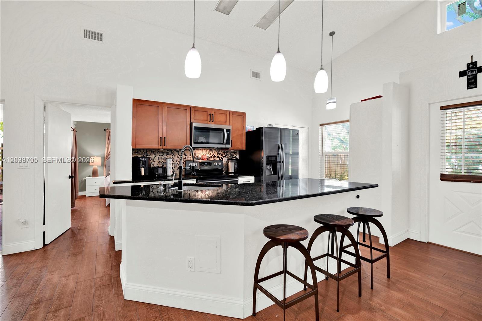 A kitchen features dark granite countertops, wooden cabinets, and three bar stools at an island — 10003 SW 223rd Ter, Cutler Bay FL 33190, CUTLER BAY, FL