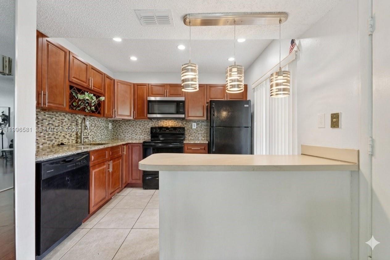 A kitchen features wood cabinets, black appliances, a tiled backsplash, and a breakfast bar — 20015 NE 3rd Ct # 6, Miami FL 33179, MIAMI, FL