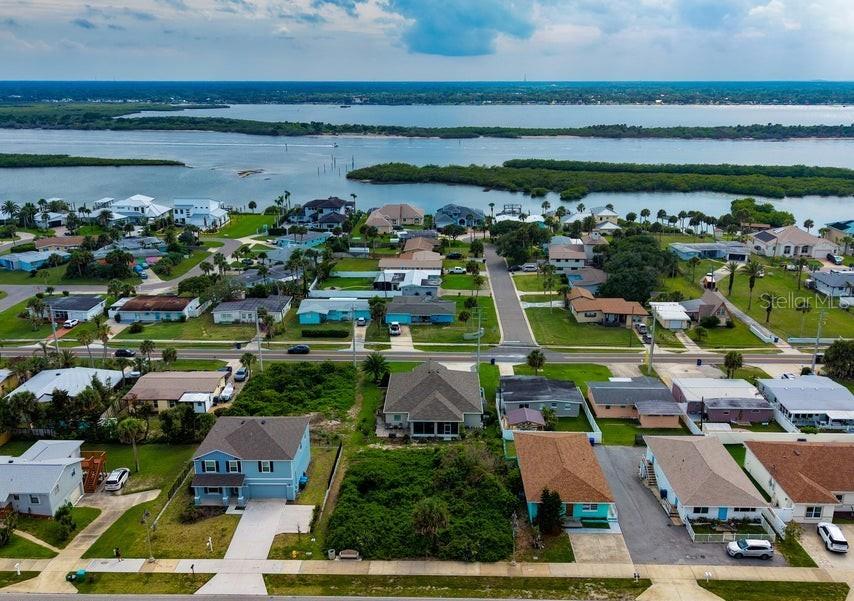 An aerial view shows a coastal neighborhood with houses, green lawns, and a nearby waterway — 3826 S ATLANTIC AVENUE, DAYTONA BEACH SHORES, FL