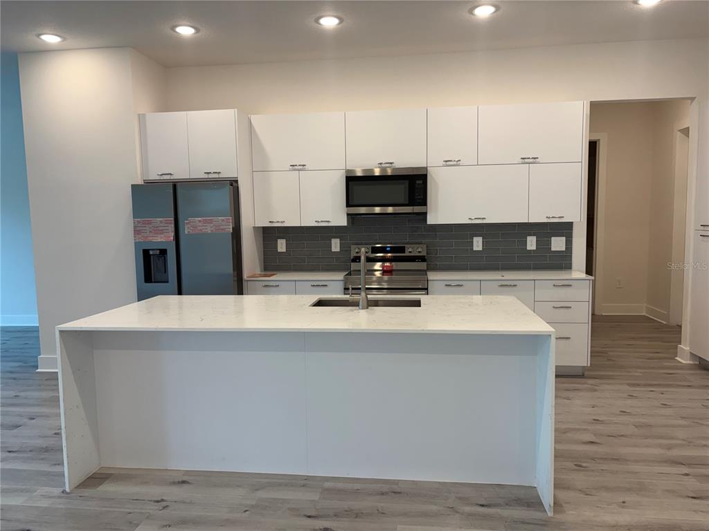 A modern kitchen features white cabinetry, a large quartz island, and a gray tiled backsplash — 14681 KEYSTONE BOULEVARD, PORT CHARLOTTE, FL