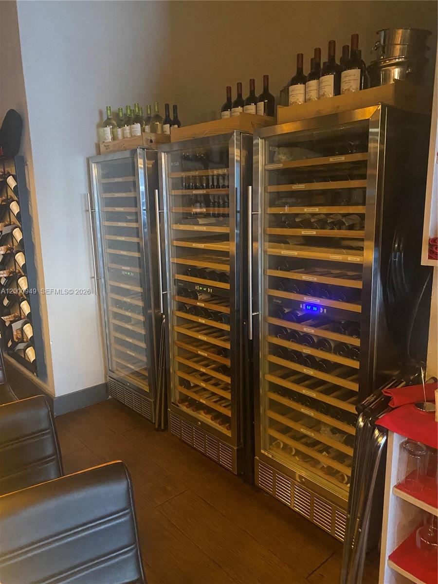 Three stainless steel wine refrigerators stand against a wall with additional bottles stored on top — 9511 S DIXIE HWY, Pinecrest FL 33156, PINECREST, FL