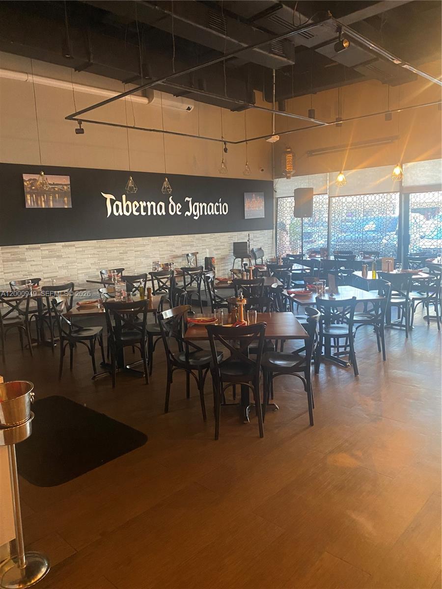 The interior of a restaurant features dark wooden tables, black chairs, and a branded wall — 9511 S DIXIE HWY, Pinecrest FL 33156, PINECREST, FL