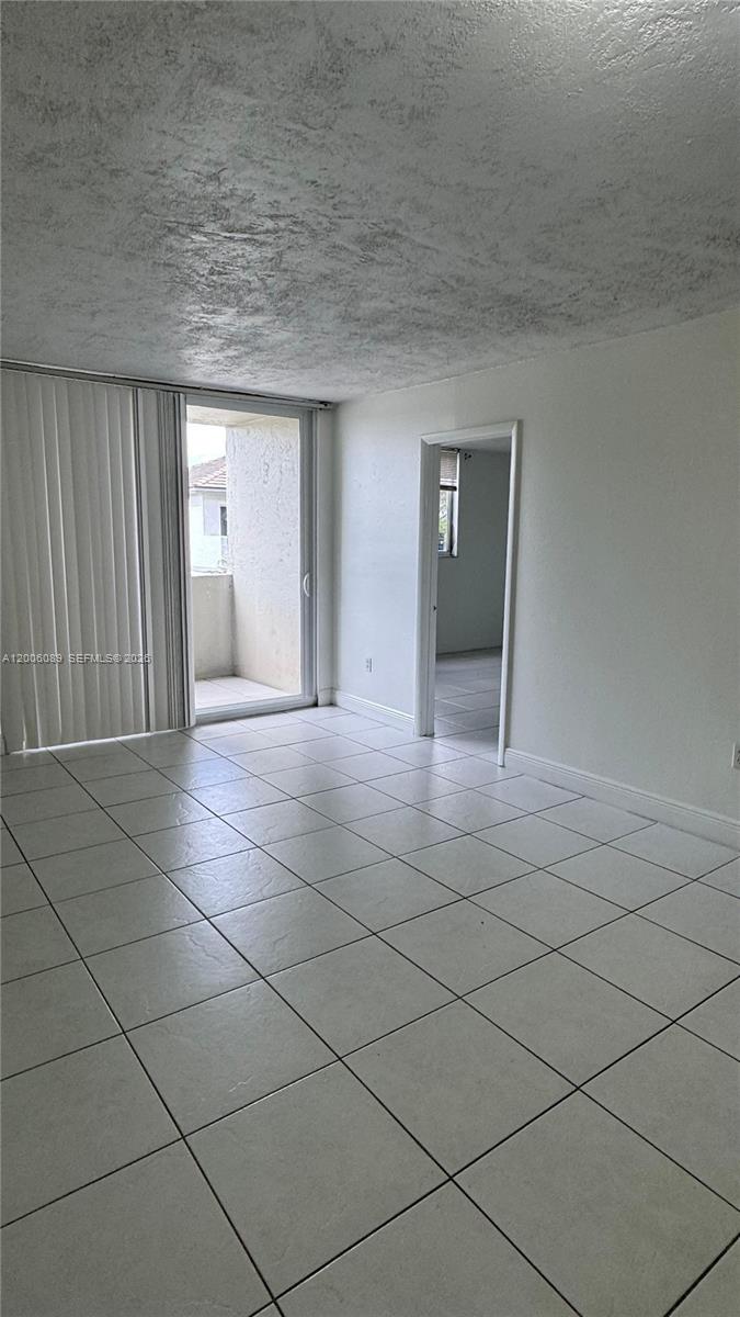 A room with white tiled floors, a sliding glass door to a balcony, and a doorway — 10090 NW 80th Ct # 1203, Hialeah Gardens FL 33016, HIALEAH GARDENS, FL