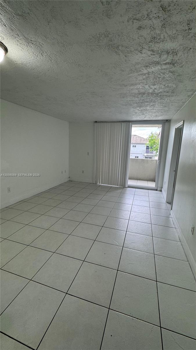 An empty room features white walls, light-colored floor tiles, and a sliding glass door to a balcony — 10090 NW 80th Ct # 1203, Hialeah Gardens FL 33016, HIALEAH GARDENS, FL