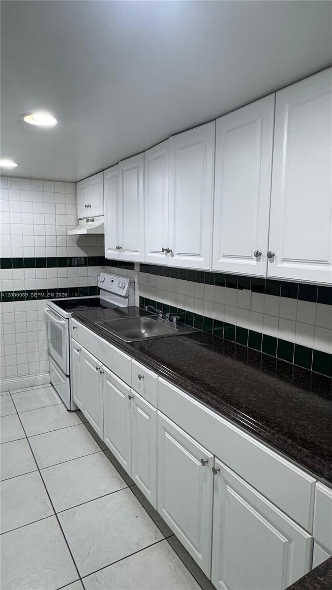 A kitchen features white cabinets, dark countertops, and a tiled backsplash with a green accent — 10090 NW 80th Ct # 1203, Hialeah Gardens FL 33016, HIALEAH GARDENS, FL