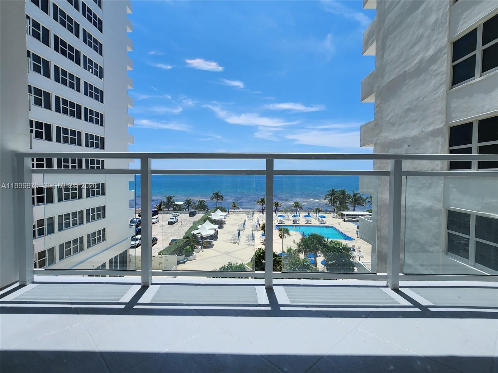 A balcony view overlooks a swimming pool, parking lot, and the ocean between two buildings — 2030 S Ocean Dr # 515, Hallandale Beach FL 33009, HALLANDALE BEACH, FL
