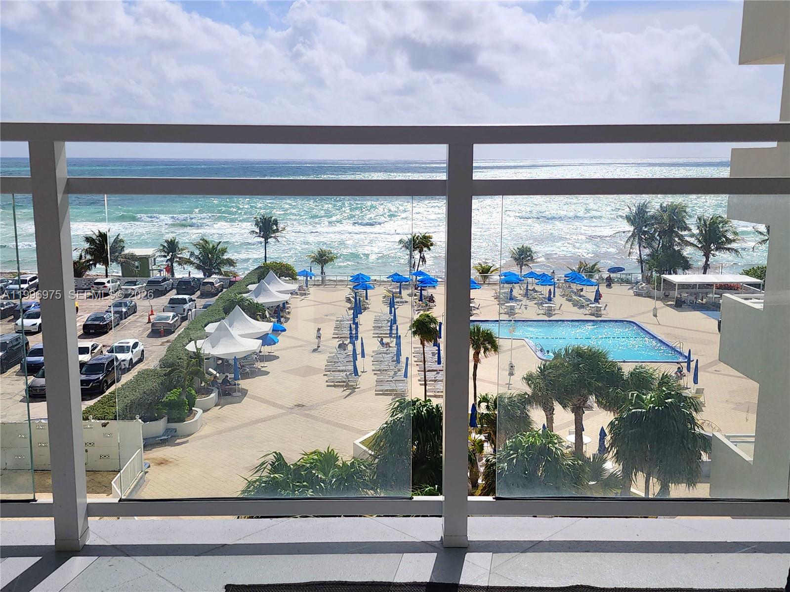 A balcony view overlooks a swimming pool, beach chairs, parking lot, and the ocean — 2030 S Ocean Dr # 515, Hallandale Beach FL 33009, HALLANDALE BEACH, FL