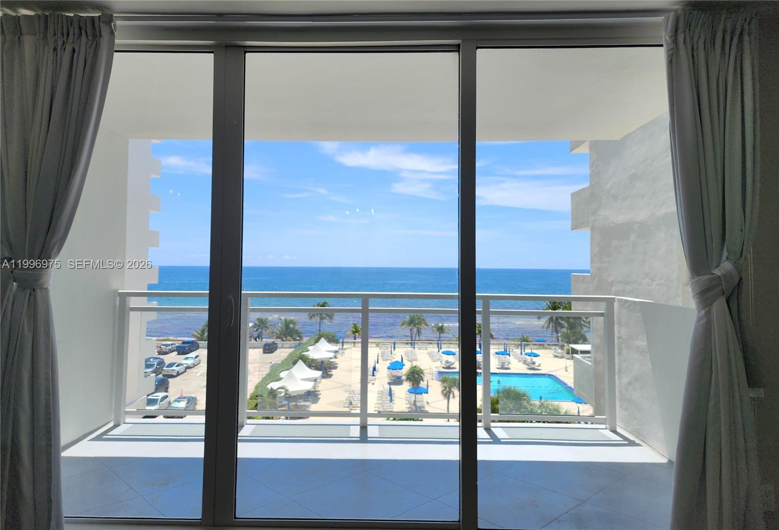 A view of the ocean, pool, and parking lot from a balcony through sliding doors — 2030 S Ocean Dr # 515, Hallandale Beach FL 33009, HALLANDALE BEACH, FL