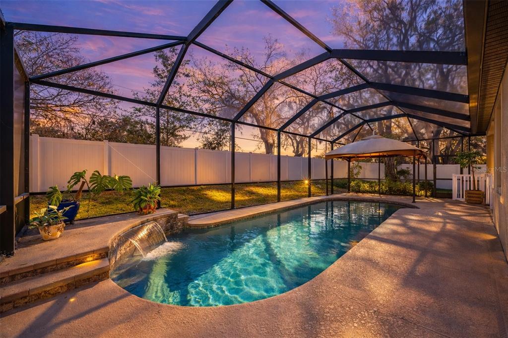 A screened-in swimming pool with a waterfall feature and a gazebo at sunset — 11652 PALMETTO PINE STREET, RIVERVIEW, FL