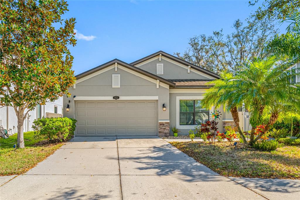 A single-story house with a two-car garage, gray stucco exterior, and a concrete driveway — 11652 PALMETTO PINE STREET, RIVERVIEW, FL