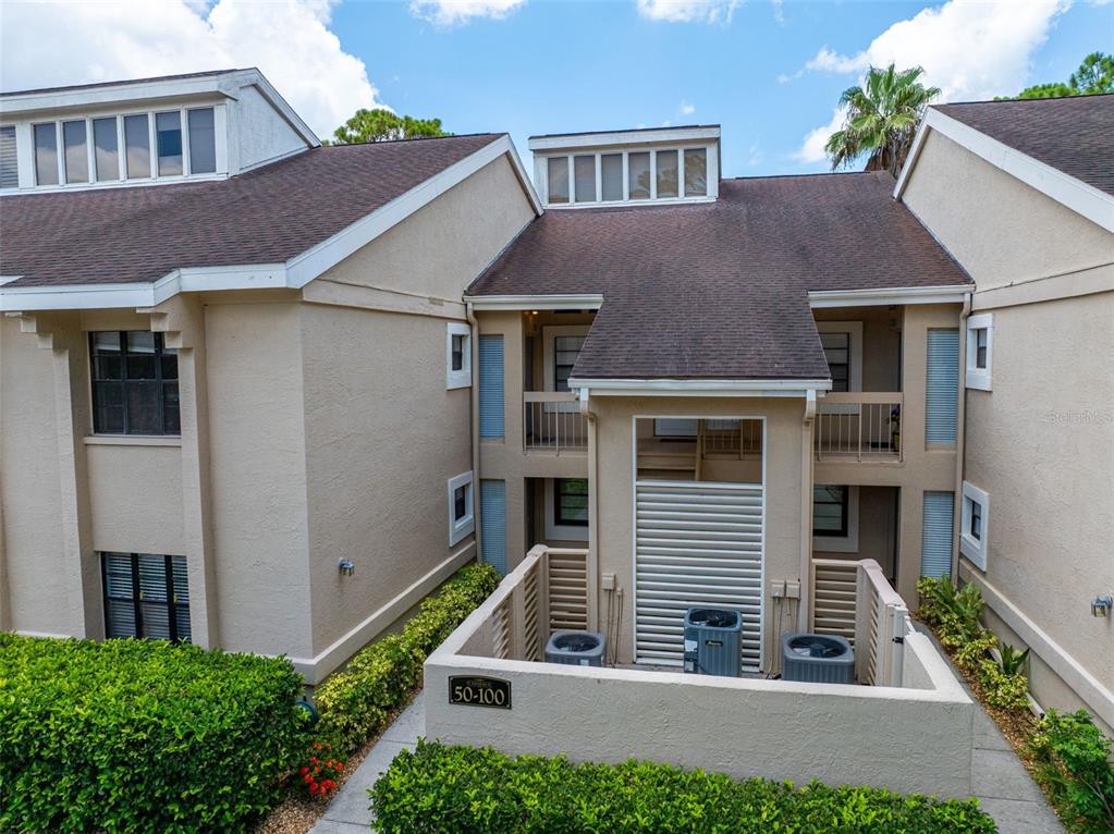 An exterior view of a multi-story tan residential building with a central courtyard and HVAC units — 60 ST ANDREWS PLACE UNIT 60, OLDSMAR, FL