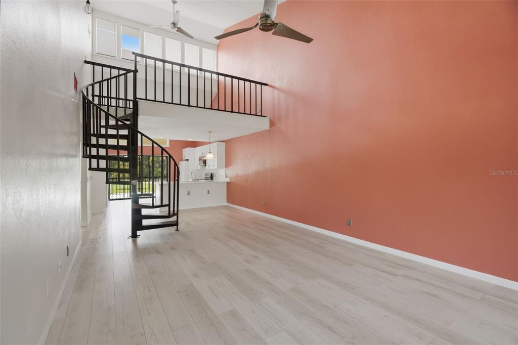 A living room with light wood floors, a spiral staircase, and a loft area — 60 ST ANDREWS PLACE UNIT 60, OLDSMAR, FL