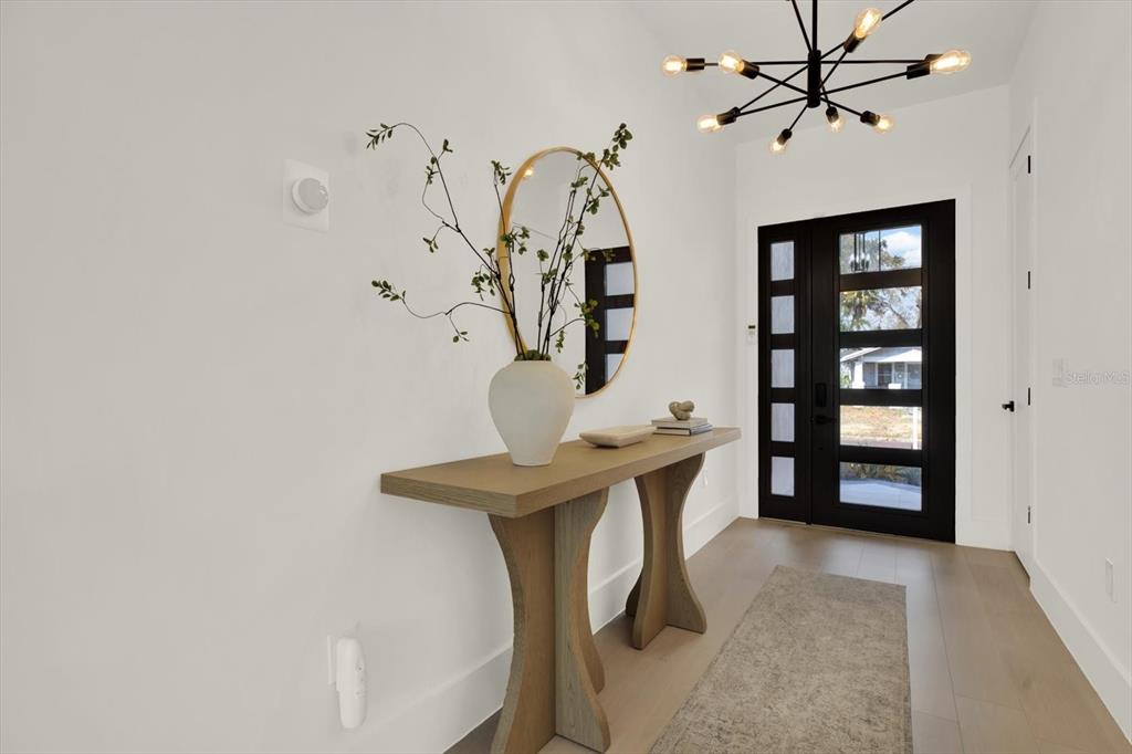 A modern entryway features a console table, round mirror, chandelier, and a black-framed glass door — 908 W FRIBLEY STREET, TAMPA, FL