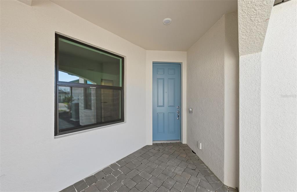 A covered entryway features a blue front door, a large window, and paver flooring — 14864 MISTY POND LOOP, NOKOMIS, FL