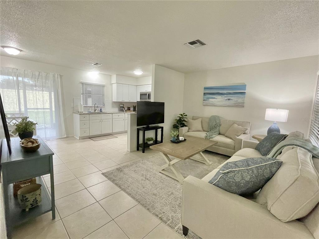 An open-concept living room and kitchen feature tile flooring, neutral walls, and light-colored furniture — 1941-1943 FORKED CREEK DR, ENGLEWOOD, FL