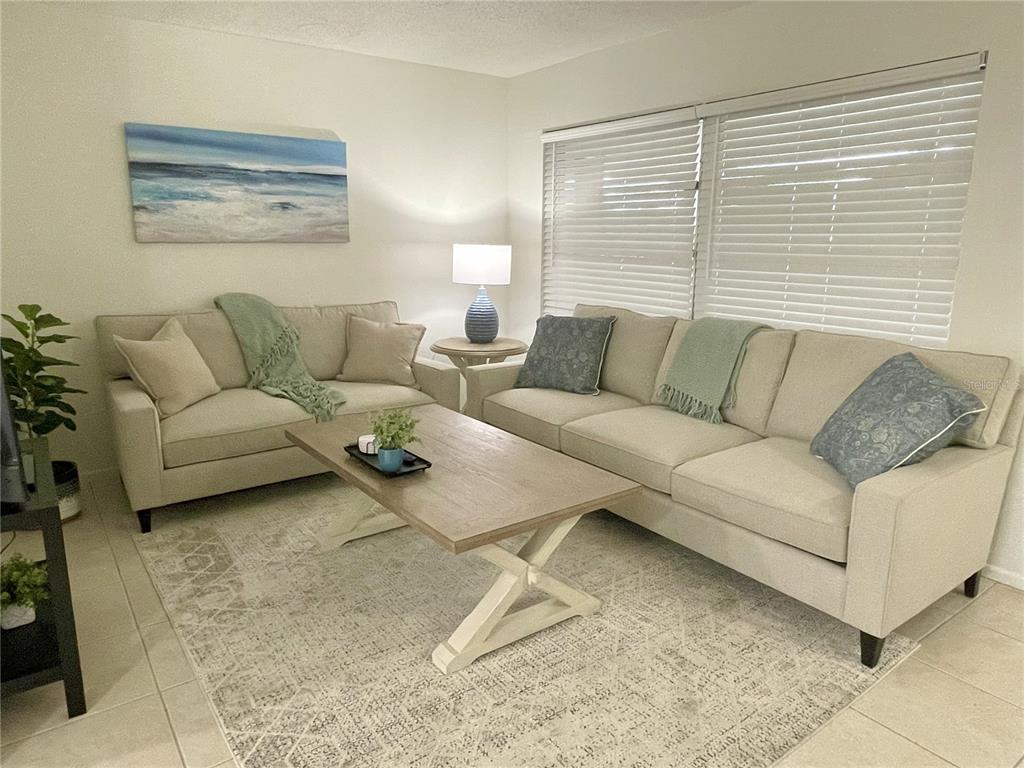 A living room features two beige sofas, a wooden coffee table, and a patterned rug — 1941-1943 FORKED CREEK DR, ENGLEWOOD, FL