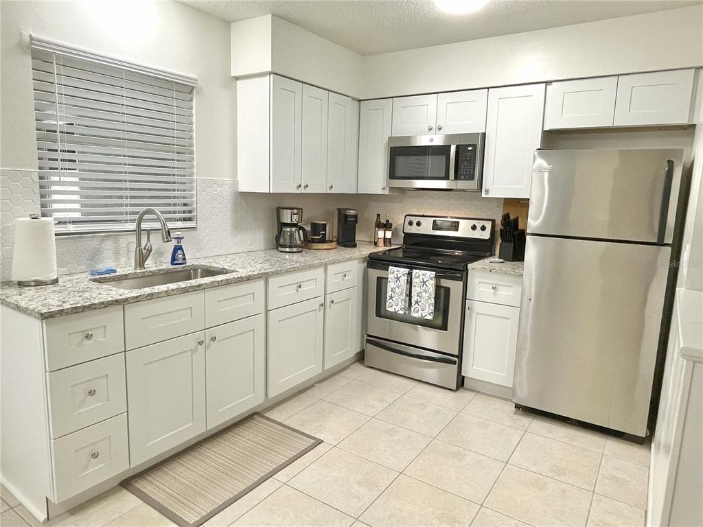 A kitchen features white cabinets, stainless steel appliances, granite countertops, and a tile floor — 1941-1943 FORKED CREEK DR, ENGLEWOOD, FL