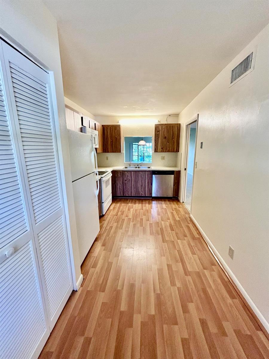 A galley kitchen features wood-look laminate flooring, dark wood cabinets, and white appliances — 2900 SW 22nd Circle # 221d, Delray Beach FL 33445, DELRAY BEACH, FL