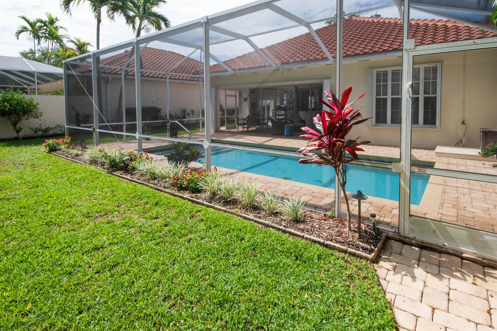 A backyard swimming pool is enclosed by a screened lanai next to a residential house — 146 Lost Bridge Drive, Palm Beach Gardens FL 33410, PALM BEACH GARDENS, FL