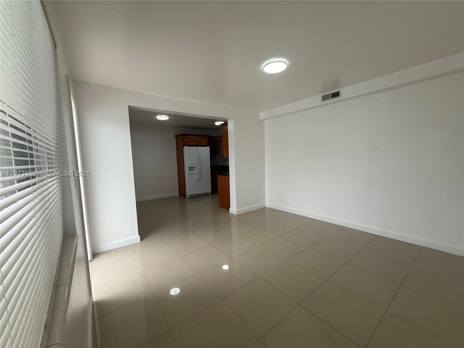 A bright, tiled living area opens into a kitchen with wooden cabinets and a refrigerator — 1122 NW 32nd Ct, Miami FL 33125, MIAMI, FL