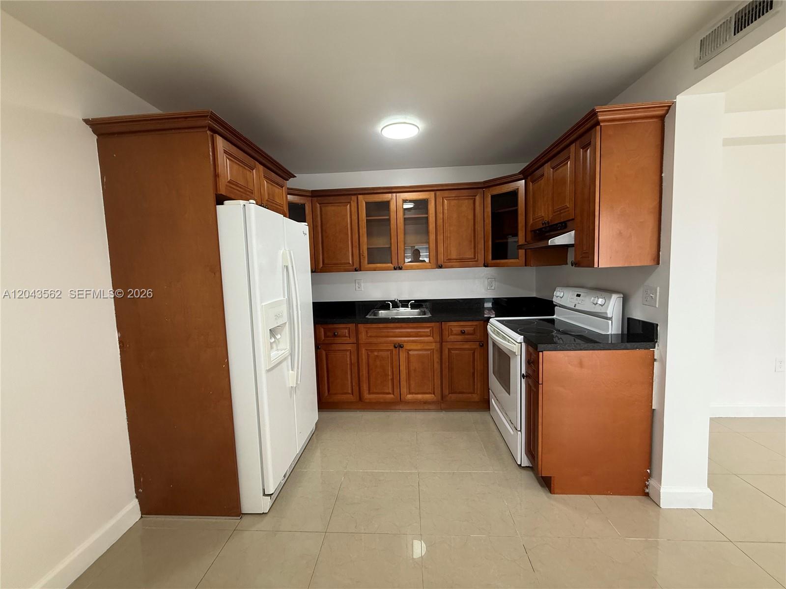A kitchen features wooden cabinets, black countertops, a white refrigerator, and a white stove — 1122 NW 32nd Ct, Miami FL 33125, MIAMI, FL