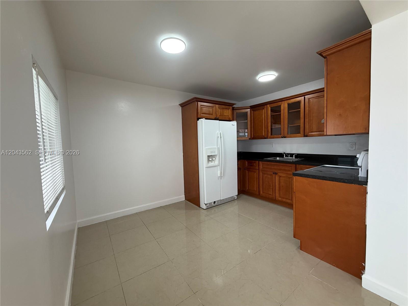 A kitchen features wood cabinets, black countertops, a white refrigerator, and light-colored tile flooring — 1122 NW 32nd Ct, Miami FL 33125, MIAMI, FL