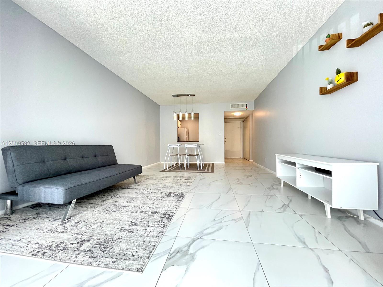 A living room features gray walls, white marble-look tile floors, a gray sofa, and floating shelves — 601 Three Islands Blvd # 314, Hallandale Beach FL 33009, HALLANDALE BEACH, FL