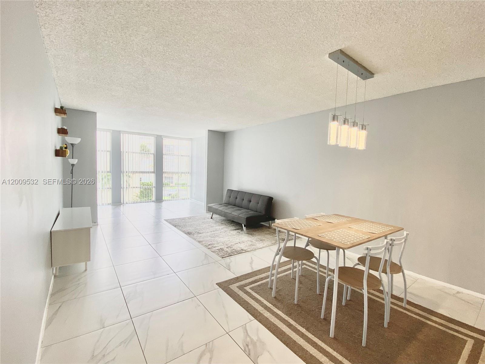 A living and dining area features white tile floors, a grey sofa, and pendant lighting — 601 Three Islands Blvd # 314, Hallandale Beach FL 33009, HALLANDALE BEACH, FL