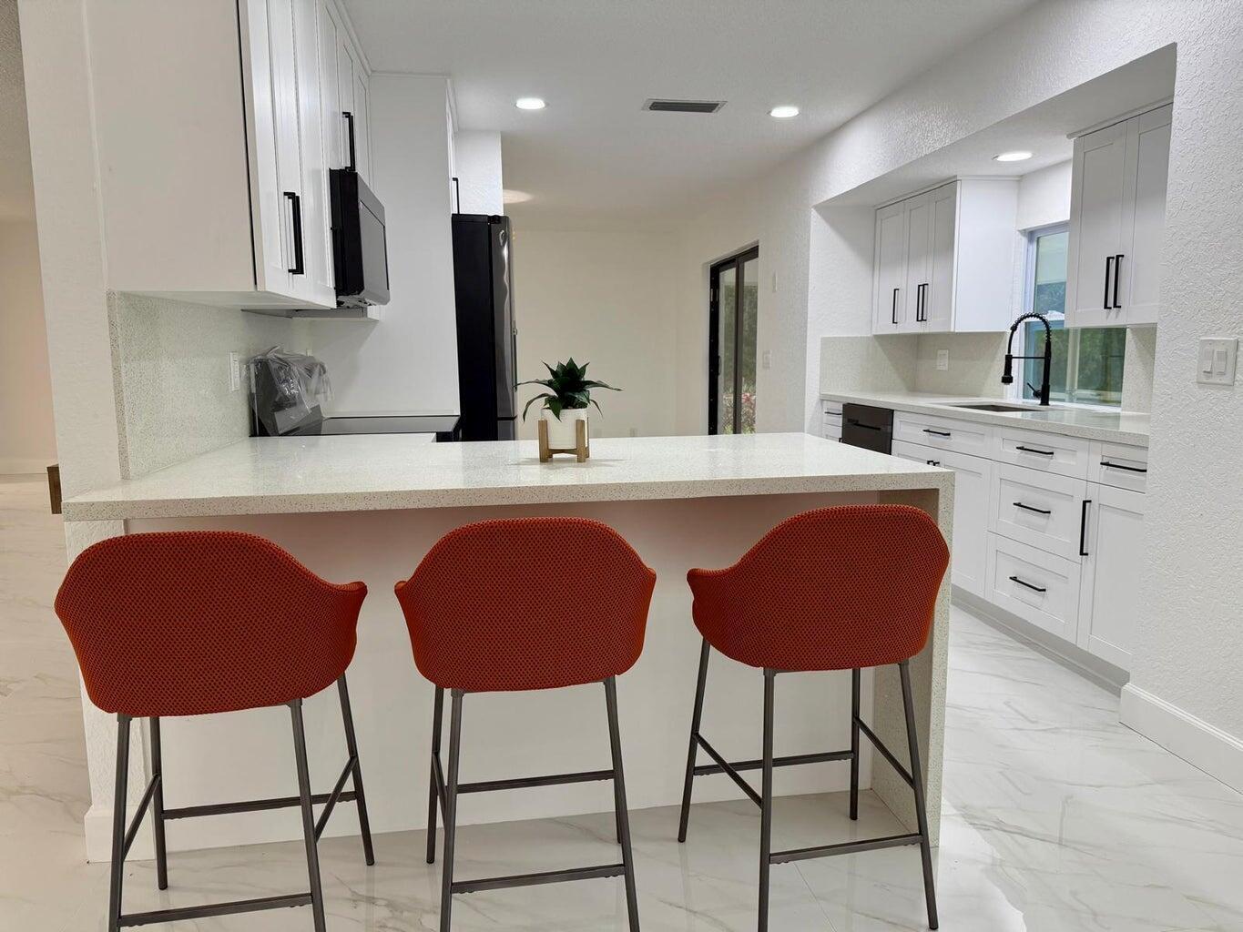 A modern kitchen features white cabinets, quartz countertops, and three orange bar stools — 2812 F Road, FL 33470, FL