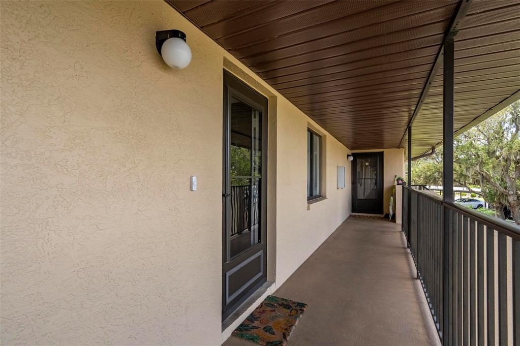A covered outdoor walkway features tan stucco walls, dark metal railings, and two glass doors — 4064 OAKVIEW DRIVE UNIT D9, PORT CHARLOTTE, FL