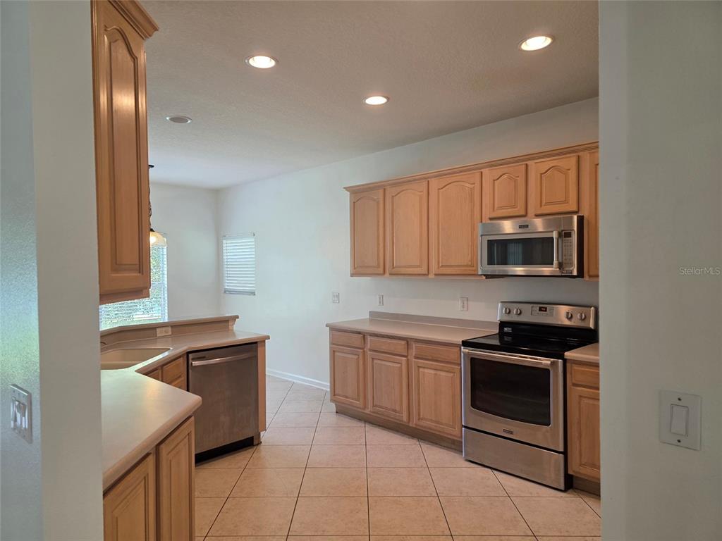 A kitchen with light wood cabinets, stainless steel appliances, and beige tile flooring — 518 FERN LAKE DRIVE, ORLANDO, FL