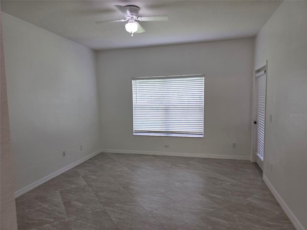 An empty room features white walls, tile flooring, a ceiling fan, and a window with blinds — 518 FERN LAKE DRIVE, ORLANDO, FL
