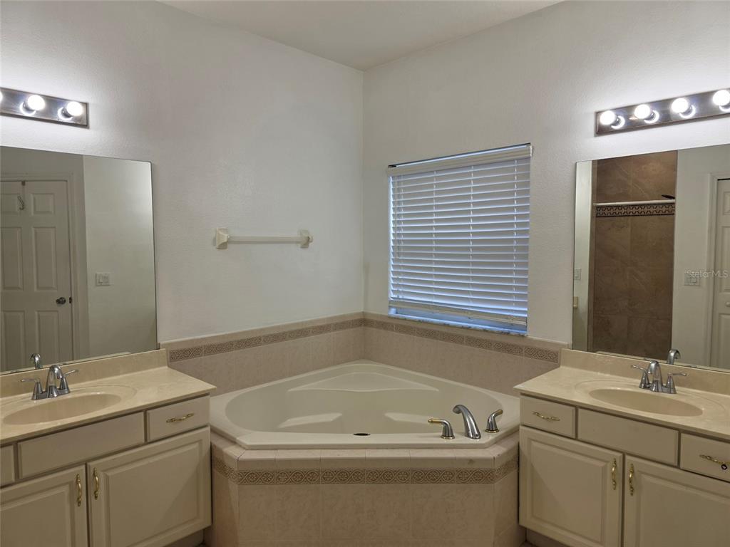 A bathroom features a corner soaking tub between two vanities with beige countertops and mirrors — 518 FERN LAKE DRIVE, ORLANDO, FL