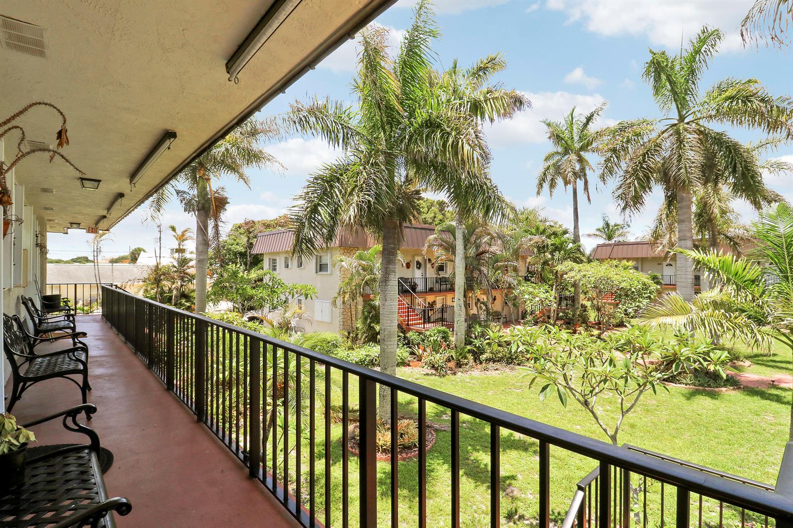 A balcony with black metal railings overlooks a grassy courtyard with palm trees and buildings — 400 Fern Street # 1c, Jupiter FL 33458, JUPITER, FL