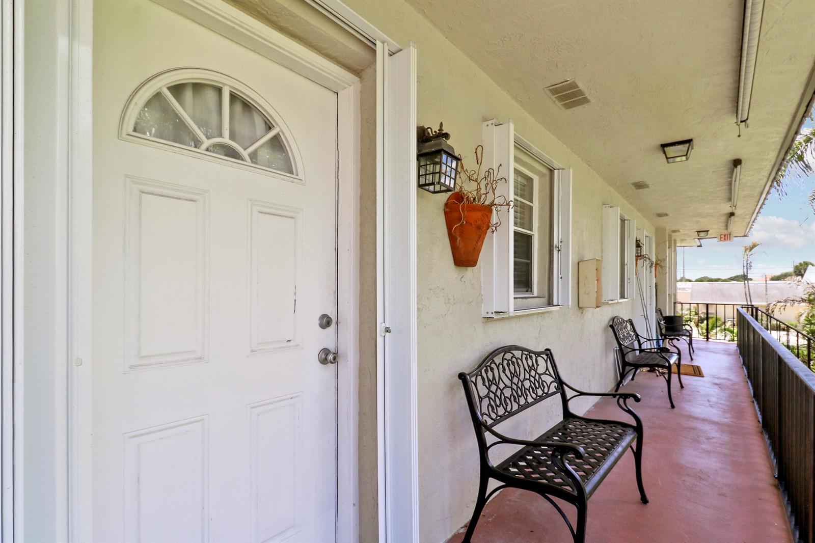 An exterior walkway features white doors, black metal benches, and a railing overlooking the outdoors — 400 Fern Street # 1c, Jupiter FL 33458, JUPITER, FL