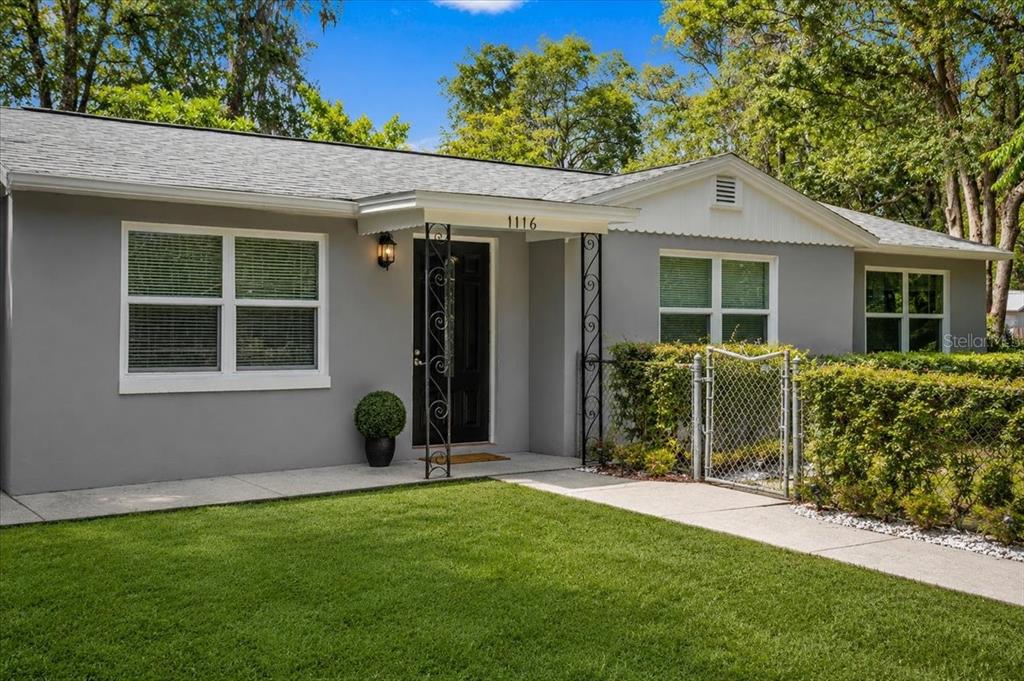 A single-story gray house features a black front door, white trim, and a chain-link fence — 1116 NW 32ND AVENUE, GAINESVILLE, FL
