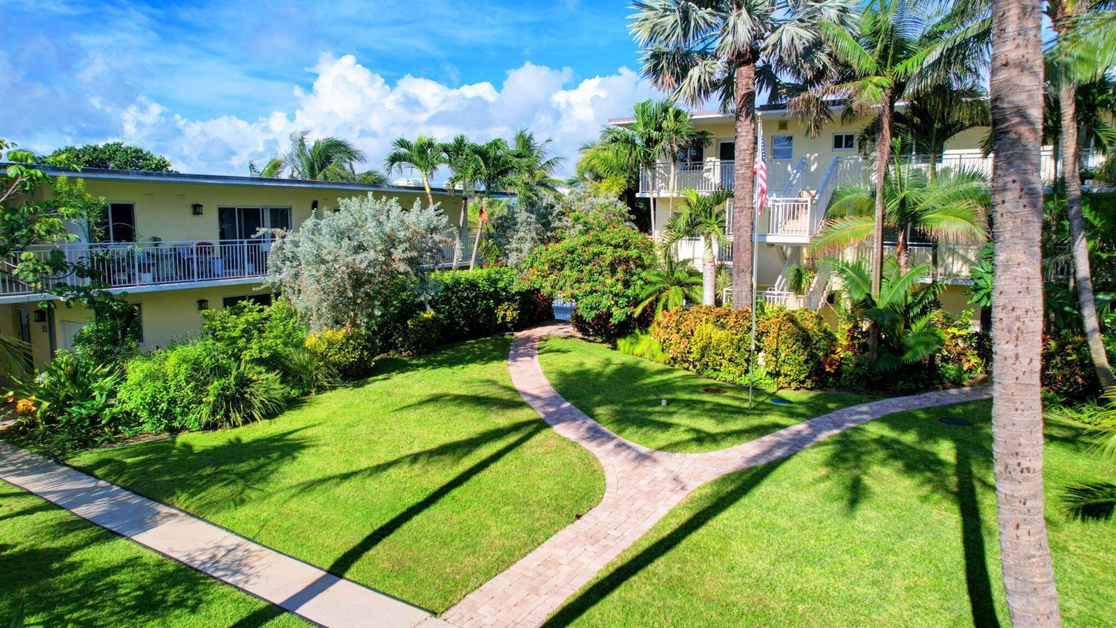 A paved walkway winds through a grassy courtyard between two multi-story apartment buildings with balconies — 6520 N Ocean Boulevard # 30, Ocean Ridge FL 33435, OCEAN RIDGE, FL