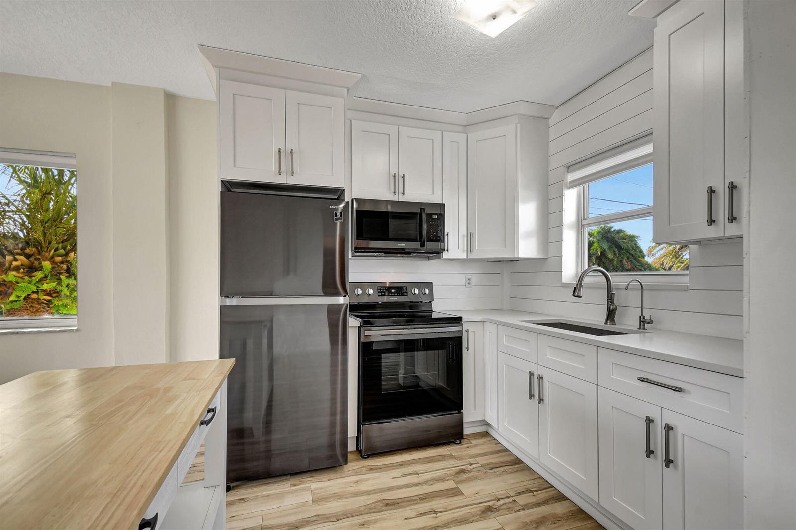 A kitchen features white cabinets, stainless steel appliances, a wood-topped island, and shiplap walls — 6520 N Ocean Boulevard # 30, Ocean Ridge FL 33435, OCEAN RIDGE, FL