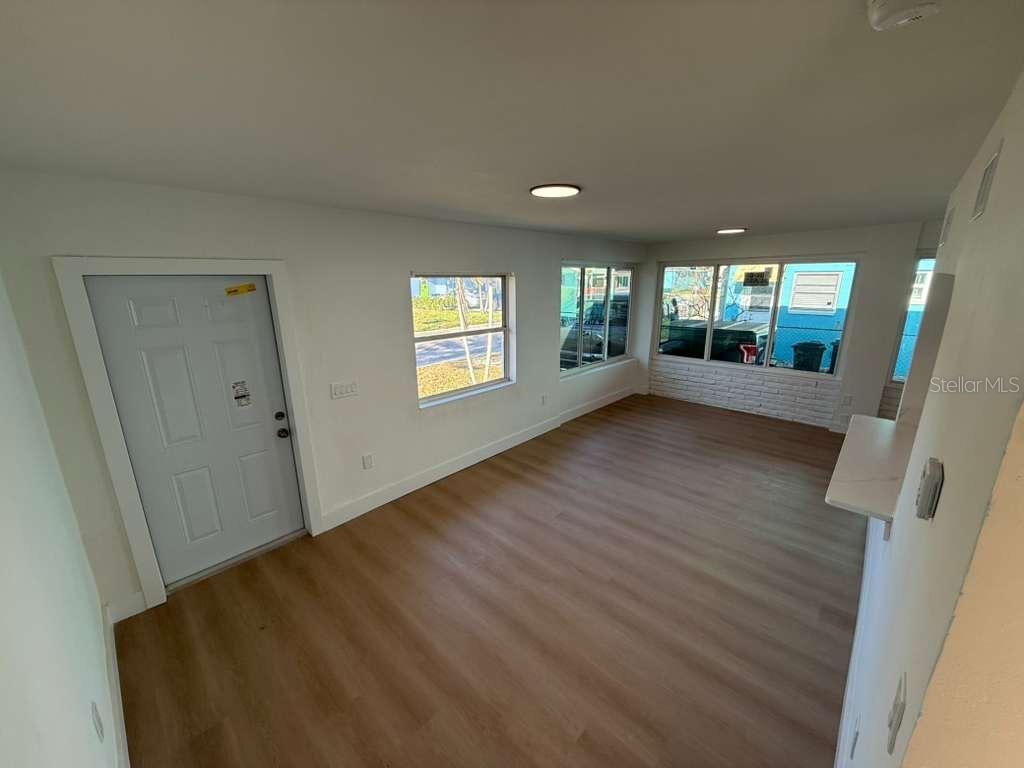 A bright living room features light wood-look flooring, white walls, and several windows — 18015 2ND STREET E, REDINGTON SHORES, FL
