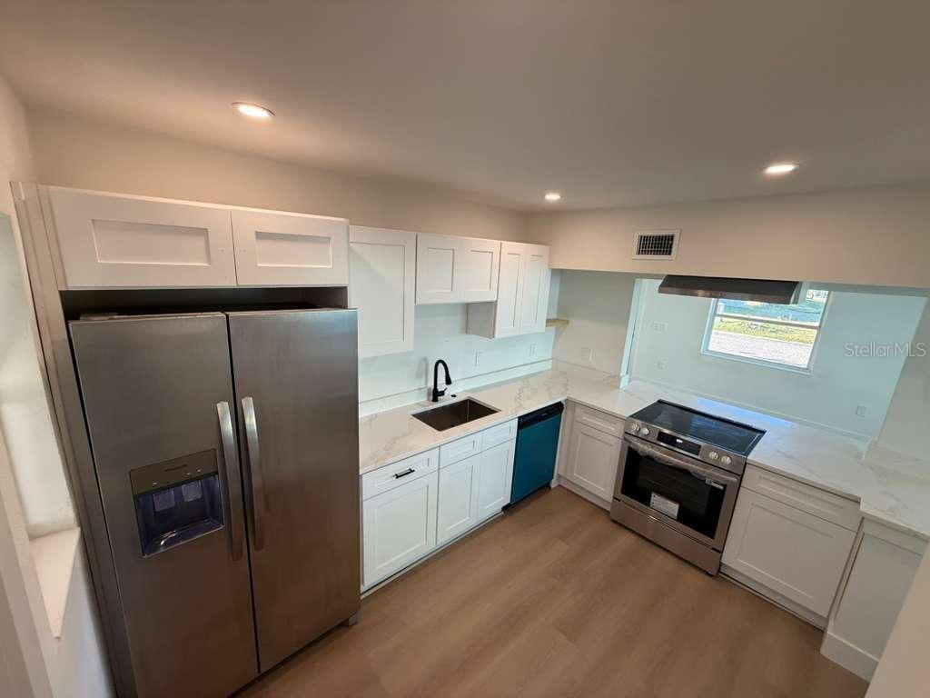 A modern kitchen features white cabinets, stainless steel appliances, and light wood-look flooring — 18015 2ND STREET E, REDINGTON SHORES, FL